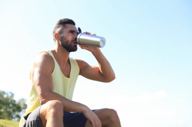 Sporcu su içiyor ve açık havada yoğun bir egzersizden sonra dinleniyor..