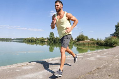 Güçlü sporcu nehir kenarında çalışırken koşuyor..