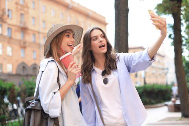 İki gülen arkadaş hafta sonunun tadını çıkarıyor ve şehrin arka planında selfie çekiyorlar.