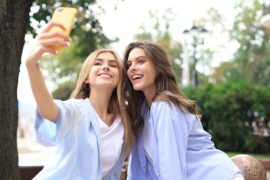 İki gülen arkadaş hafta sonunun tadını çıkarıyor ve şehrin arka planında selfie çekiyorlar.