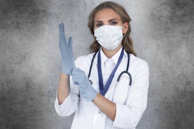 Coronavirus 'a karşı tıbbi personel önleyici ekipman. Steteskoplu kadın doktor gri arka planda izole edilmiş tıbbi eldiven takıyor.