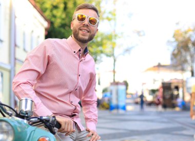 Yakışıklı adam bir tatil bağlamda bir scooter üzerinde poz. Sokak moda ve stil