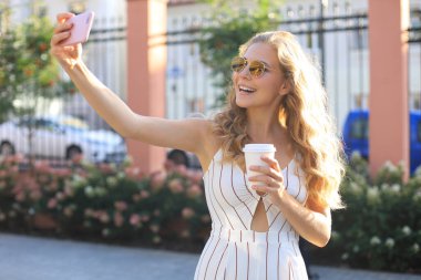 Mutlu genç sarışın kadın, açık havada kendi portresini yaparken gülümsüyor.