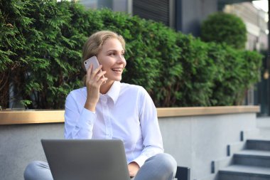 Ofisin yakınında telefon ve dizüstü bilgisayarla çalışan mutlu bir girişimci.