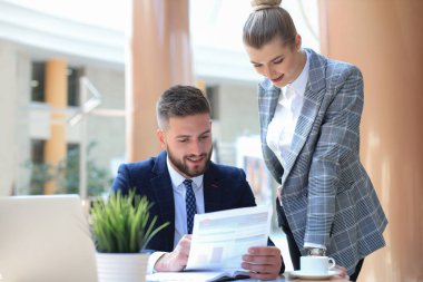 Başlangıç projesinde işbirliği yaparken ofiste dizüstü bilgisayar kullanan iki genç iş adamı