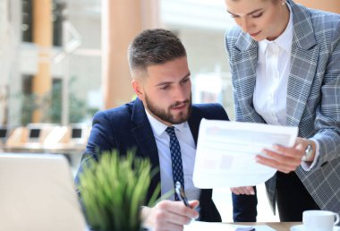 Başlangıç projesinde işbirliği yaparken ofiste dizüstü bilgisayar kullanan iki genç iş adamı