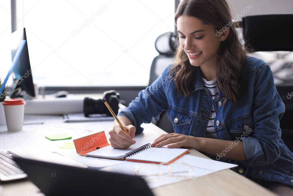 Happy young woman writing something down while working in the office