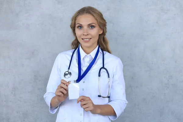 Usmívající Blondýnka Lékař Uniformě Stojící Izolovaně Nad Šedým Pozadím Ukazující — Stock fotografie