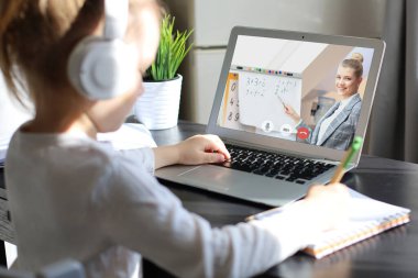 Mesafe öğrenme. Kulaklıklı neşeli küçük kız bilgisayarını kullanarak internetten e-öğrenim sistemini inceliyor.