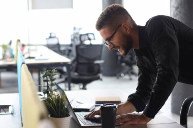 Genç modern iş adamı ofiste çalışırken dizüstü bilgisayarla veri analiz ediyor..