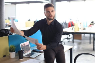 Genç adam ofiste otururken kağıtlarla uğraşıyor..