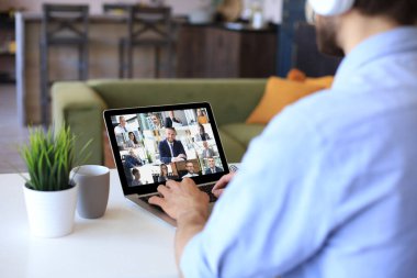 Kulaklıklı bir iş adamı, iş arkadaşlarıyla video konuşmasında kişisel tecrit ve karantina sırasında online brifing hakkında konuşuyor. Ofisteki iş arkadaşlarıyla webcam grup konferansı.
