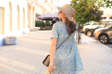 Gülümseyen hippi moda kızı, elinde şapkayla, yaz caddesinde poz veriyor.
