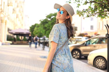 Gülümseyen hippi moda kızı, elinde şapkayla, yaz caddesinde poz veriyor.