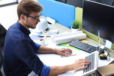 Ofisinde tasarım üzerinde çalışan yakışıklı bir erkek mimarın fotoğrafı.