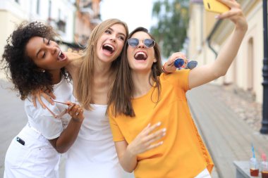Üç tatlı kız arkadaş birlikte eğleniyor, şehirde selfie çekiyorlar.