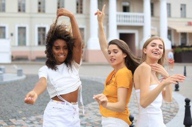 Sokakta poz veren üç genç, gülümseyen hippi kadın. Olumlu yüz ifadeleri sergiliyor. Dans etmek.
