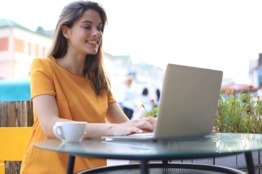 Kafede dizüstü bilgisayar kullanan gülümseyen bir kadın. Girişimci, iş kadını, serbest çalışan kavramı