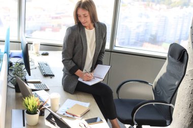 Yoğunlaşmış genç bir kadın ofiste çalışırken bir şeyler yazıyor.