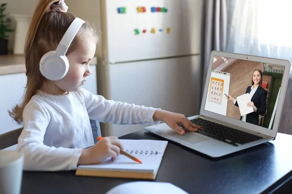 Distance learning. Cheerful little girl girl in headphones using laptop studying through online e-learning system.