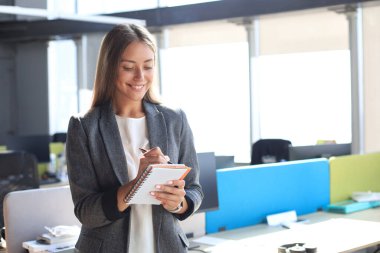 Yoğunlaşmış genç bir kadın ofiste çalışırken bir şeyler yazıyor.