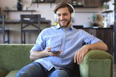 Çekici bir genç adam evdeki koltukta dinleniyor ve e-postaları kontrol etmek için cep telefonunu kullanıyor.