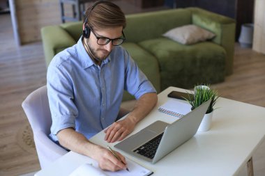 Konsantre genç serbest çalışan işadamı video konferansı için dizüstü bilgisayar kullanıyor, evde uzaktan çalışıyor.