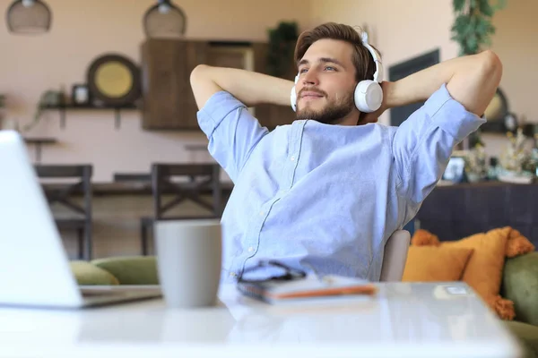 Smiling businessman freelancer in earphones leaning back in chair with hands behind head and dreaming about new opportunities in business