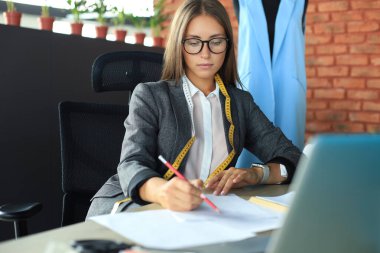 Güzel genç tasarımcı stüdyosunda otururken notlar alıyor.