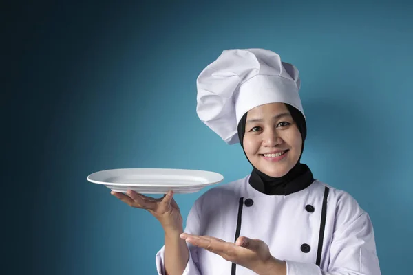 Azji kobieta szef kuchni pokazuje pusty biały talerz, prezentując coś, — Zdjęcie stockowe