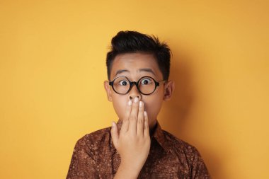 Şaşırmış Asyalı çocuk, elleriyle ağzını kapatıyor.