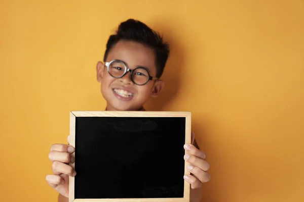 Inteligente asiático chico sonriendo en cámara y mostrando vacío pizarra — Foto de Stock