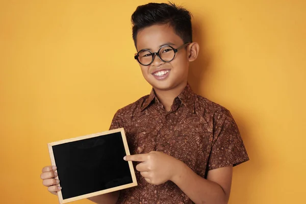 Inteligente asiático chico sonriendo en cámara y mostrando vacío pizarra — Foto de Stock