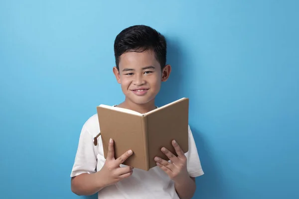 Asiatisk pojke ler glatt när han läser en bok — Stockfoto