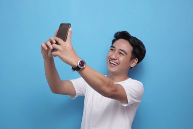 Mutlu genç adam telefonla selfie çekiyor.