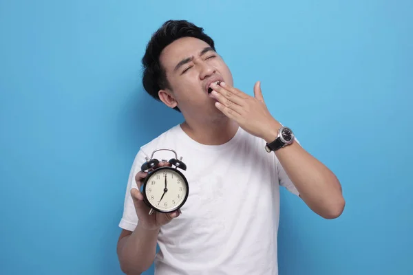 Genç Asyalı adam çalar saati tutarken yorgun ve esniyor. — Stok fotoğraf