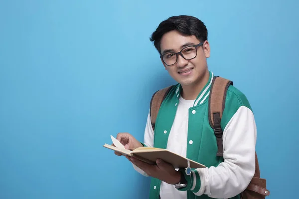 Hombre Asiático estudiante sonriendo y leyendo un libro sobre fondo azul — Foto de Stock