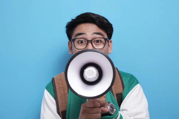 Молодой азиатский студент в зеленой бейсбольной куртке кричит на мегафон — стоковое фото
