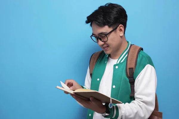 Bărbat asiatic student zâmbind și citind o carte pe fundal albastru — Fotografie, imagine de stoc
