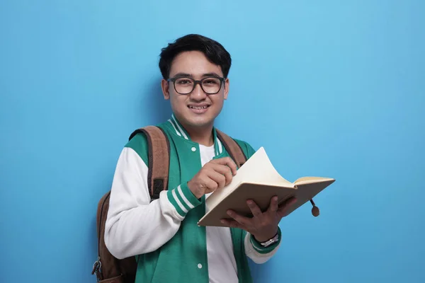 Hombre Asiático estudiante sonriendo y leyendo un libro sobre fondo azul — Foto de Stock