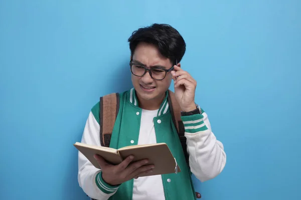 Estudiante asiático masculino estudiando duro, leyendo un libro sobre fondo azul — Foto de Stock