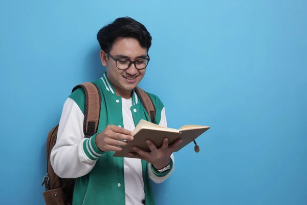 Homme asiatique étudiant souriant et lisant un livre sur fond bleu — Photo