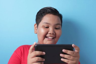 Fat Asian boy plays online game on his tablet gadget