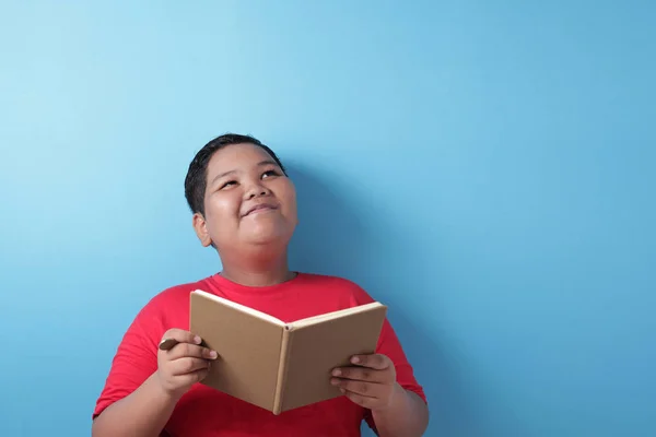 Товстий азіатський хлопчик, який шукає вираз мислення, читаючи боо. — стокове фото