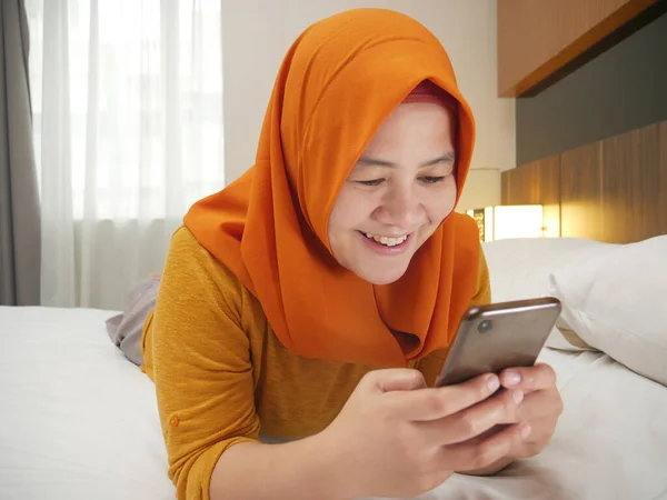 Szczęśliwa azjatycka muzułmanka w hidżabie uśmiechnięta podczas czytania tekstu — Zdjęcie stockowe