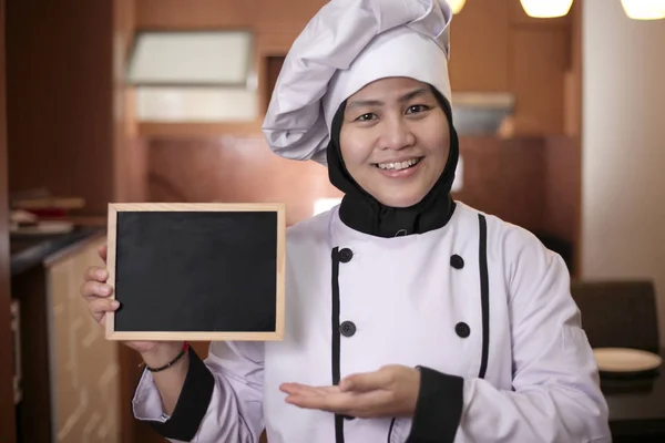 アジアの女性シェフが空のBlackboardを表示し、空白の書き込みを提示 ストック画像