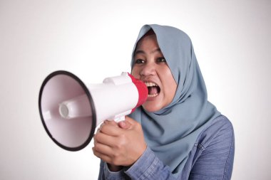 Genç Asyalı Müslüman iş kadını tesettürlü kızgın bir ifadeyle megafonda bağırıyor.