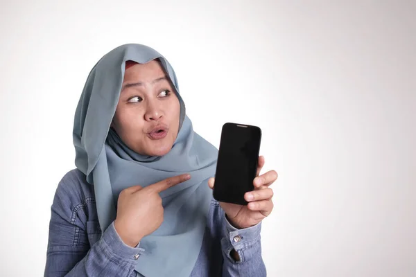アジアのイスラム教徒の女性は スマートフォンを持ちながら笑顔で 何かを提示し 側面にTiを指して — ストック写真