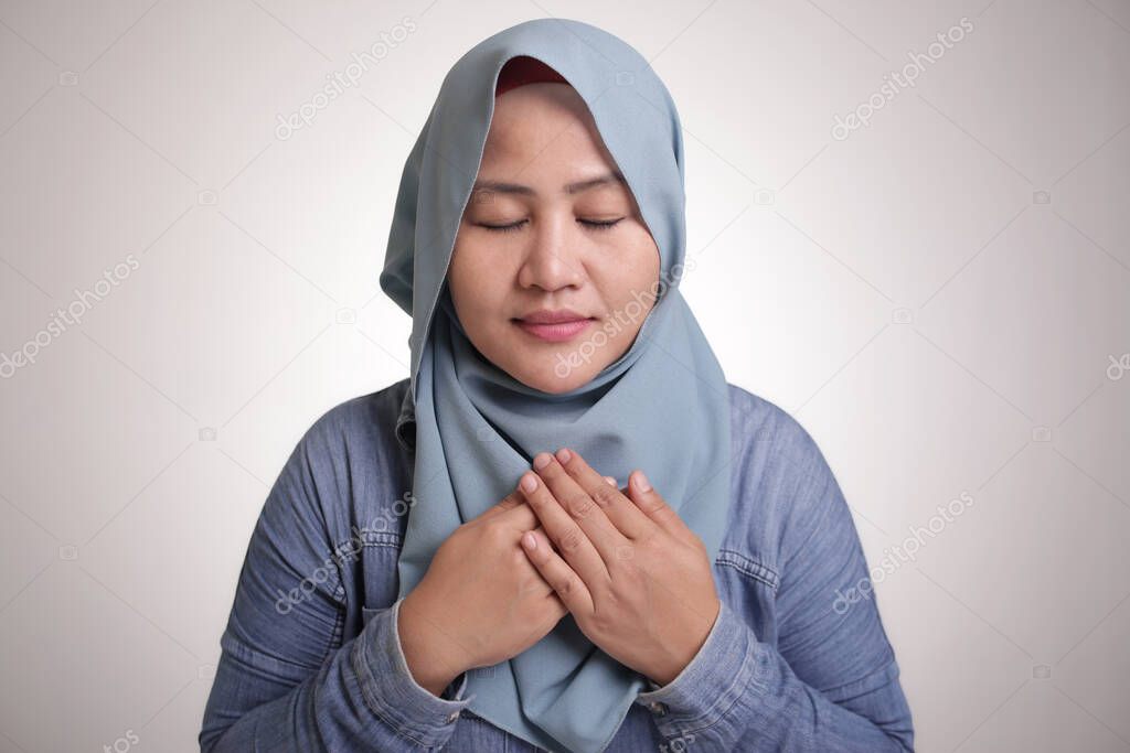 Portrait of muslim woman closing her eyes, smiling, hands on heart and pray