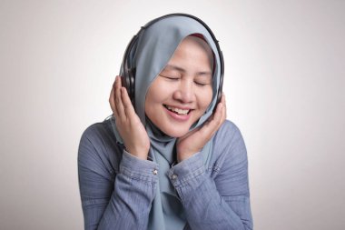 Güzel Asyalı Müslüman bir kadının portresi tesettür takıyor, kulaklıkla müzik dinliyor, dans ediyor.